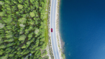 Aerial view of mountain curve road with red car. Aerial view of road between green  forest and blue...