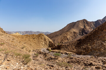 Hajar Mountains landscape in Hatta, United Arab Emirates, seen from a hiking trail, with harsh climate, dry, rocky mountain slopes and dwarf trees and bushes.