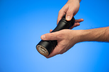 Wooden black pepper  grinder mill held by Caucasian male hands studio shot isolated on blue background