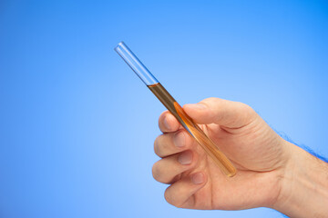 Medical glass tube with dark liquid held in hand by Caucasian male hand studio shot isolated on blue background