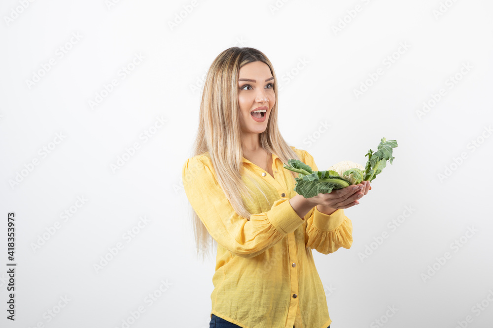 Wall mural Picture of a pretty woman model standing and holding cauliflower in hand