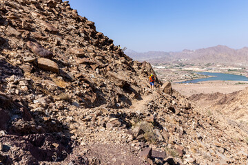 Fototapeta na wymiar Male tourist hiking on a Hatta mountain sign hike trail in Hatta, Hajar Mountains. Arid landscape with Hatta town below, United Arab Emirates.