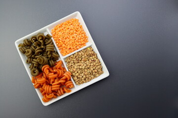 Green and red trotolle pasta, green and red lentils in a square plate. Colored pasta and lentils on a gray background. 