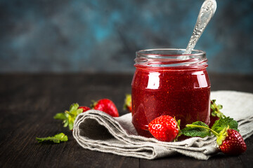 Strawberry jam in the glass jar with fresh berries at wooden table.
