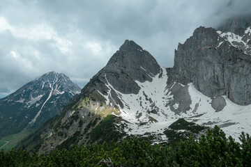 Obraz premium A panoramic view on the Alpine peaks in Austria from Marstein. The slopes are mostly covered with snow. Stony and sharp mountains. Overcast. Baren slopes, green valley below. Serenity and calmness