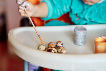 Baby paints easter quail eggs on at kindergarden. Happy Easter concept. The child develops fine motor skills with bright paints. Cope space