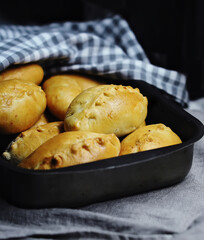 homemade little stuffed pies (patties) in metal dish side view on black background closeup. Selective focus