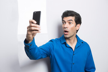 uomo moro in camicia blu fa una foto con il suo smartphone, isolato su sfondo su sfondo bianco