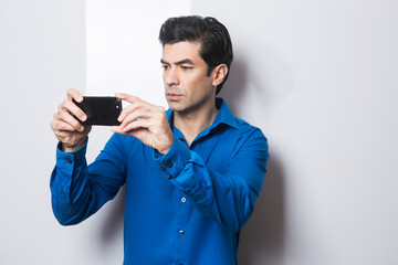 uomo moro in camicia blu fa una foto con il suo smartphone, isolato su sfondo su sfondo bianco