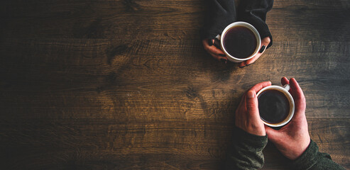 Cups of black tea or coffee in the hands of men and women. on a wooden background. with copy space....
