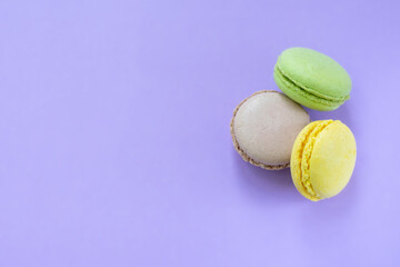 Three colorful french traditional biscuits also known as macarons on light purple background. Yellow, brown and green round cookies