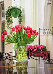 Fototapeta na wymiar A glass vase with a bouquet of red tulips stands on the lid of a piano