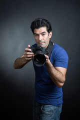 fotografo moro in maglietta blu e fotocamera al collo è pronto a fare una foto  , isolato su sfondo nero