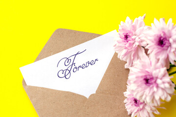 Love envelope and letter with written word forever with pink chrysanthemum flowers on bright yellow bacground.