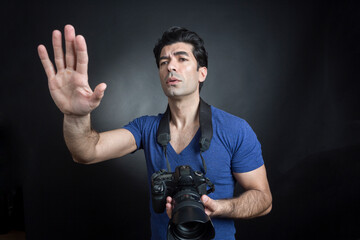 fotografo moro in maglietta blu e fotocamera al collo fa una foto e da delle indicazioni a qualcuno , isolato su sfondo nero