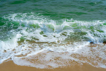 The blue sea waves lapping yellow sands and clear green water. 