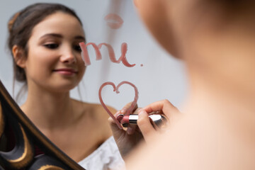 Blurred photo of a young girl posing in front of a mirror. Heart with lipstick on the mirror.