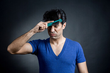 uomo moro in maglietta blu si pettina i capelli con espressione contrariata, isolato su sfondo nero