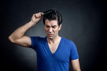 uomo moro in maglietta blu si pettina i capelli con espressione contrariata, isolato su sfondo nero