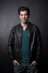 Fototapeta premium Uomo moro con maglietta verde, giacca in pelle e jeans, guarda con espressione contrariata, isolato su sfondo scuro