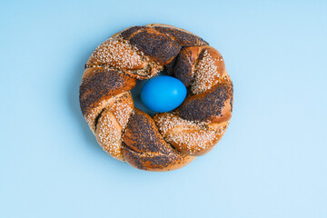 Homemade Easter bread ring with handmade dyed egg on light blue background
