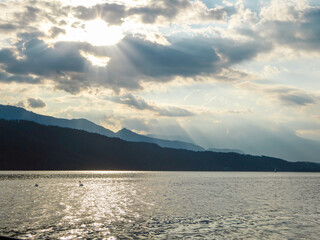 A pair of swans landing on Millstaetter lake in Austria during the sunset. The lake is surrounded by high Alps. Calm surface of the lake reflecting the sunbeams. The sun sets behind the mountains