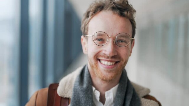 Close-up of the face of a young blond guy with glasses smiling at the camera