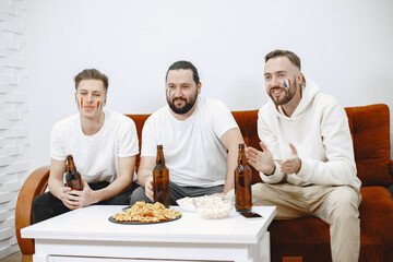 Fans sitting on the couch in the living room. Guys drinking a beer.