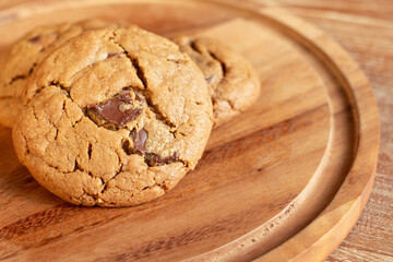 Delicious Homemade Chocolate Chip Cookies. Chocolate chip cookies on plate on wooden background. Warm, golden brown, chocolate chip cookies cooling on baking paper. Natural handmade organic cookies.