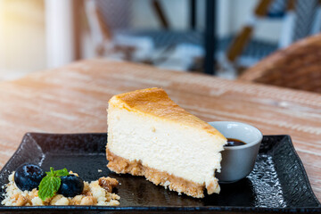Cheesecake slice. New York style classic cheesecake on wooden background. Slice of new york style cheesecake on black plate with blueberry sauce. Cheesecake slice on black plate on wooden table.