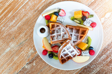 Fototapeta na wymiar Belgian waffles with fresh fruit and caramel on white plate on wooden table. Foster Waffle with whipped cream and fruits on wooden table. Homemade waffles with mixed berry fruits.