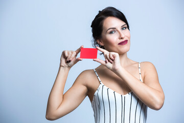 Donna bianca con i capelli neri  vestita  con una tuta bianca a righe mostra una card rossa ,...