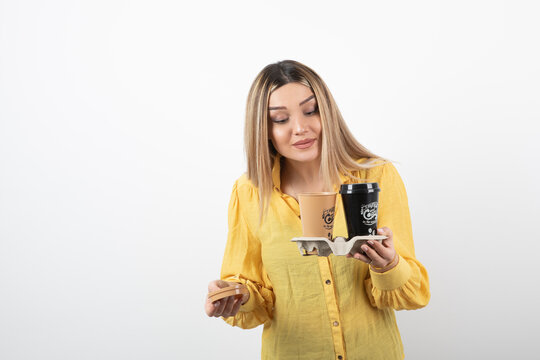 Image of young person holding cups of coffee and looking at lid