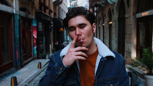 A young pretentious man smoking on the narrow street