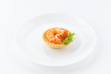 Tartlet with shrimp, tomato and cheese on a white plate.