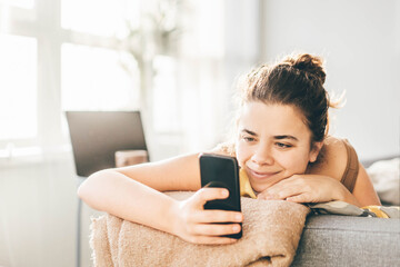 Happy young woman using smartphone on couch.