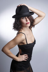 Bellissima ragazza mora con un abito nero e cappello nero posa  isolata su sfondo bianco.