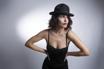 Bellissima ragazza mora con un abito nero e cappello nero posa  isolata su sfondo bianco.