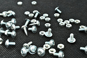 Light-colored bolts and nuts are scattered on the dark surface of the table, close-up. High quality photo