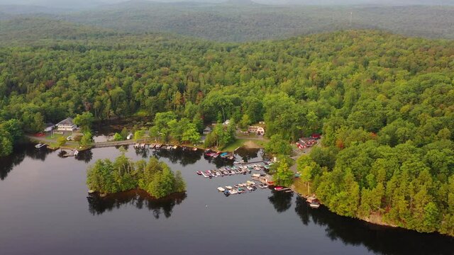 Aerial shot of boats moored at harbor on lake by trees, drone descending forward towards lush green forest - Berkshire County, Massachusetts