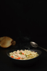 Chicken soup with vegetables, spices and homemade noodles on a dark table. Healthy food concept. Selective focus. Steam rises above the soup plate