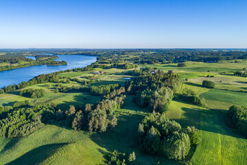 A large lake with blue water surrounded by numerous hills, forests and fields on the landscape from a drone.
