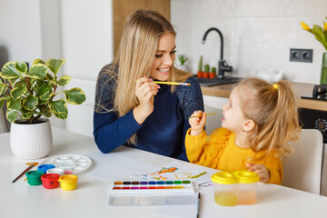 Mother and daughter painting at home. Cute little kid in yellow sweater having fun with parent and...