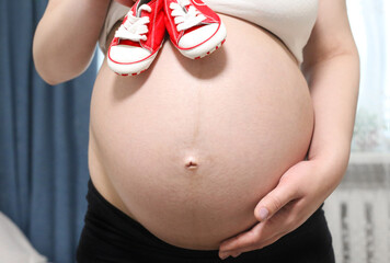 Pregnant woman holding baby sneakers on her belly.Prenatal pregnant women planning calendar for baby, Preparing utensils for pregnancy concept.
