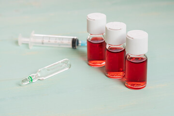 medical vaccine vials with red liquid and syringe over green table. Vaccination and immunization conceptual.
