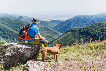 A young hiker and his Vizsla dog hiking to the top of a mountain