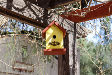 A yellow wooden birdhouse hanging on a lattice patio cover.