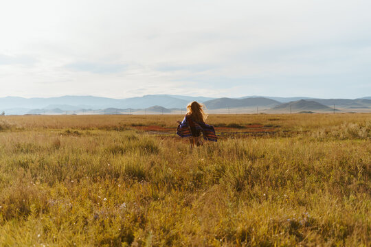 far away on the steppe grass towards the hills runs barefoot girl with a cape on her shoulders. High quality photo