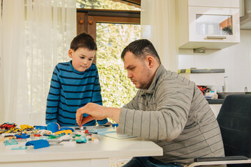 Boy playing with his father in the kitchen. Child builds something out of small parts. Little boy is playing with a parent. Father son relationship 
