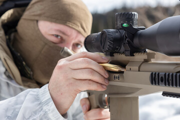 Army Man wearing Tactical Uniform with Sniper River Camouflaged in Snow Aiming at the Target. Winter Warfare. Taken in British Columbia, Canada.